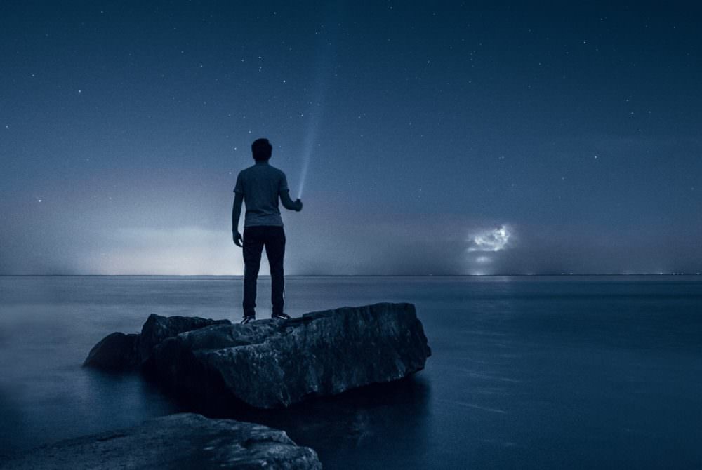 Person shining a flashlight into the sky at the beach